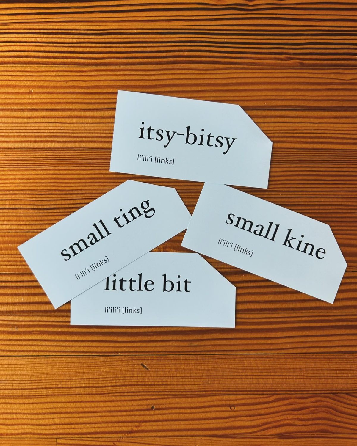Four paper tags on a wood table reading small ting, itsy-bitsy, little bit and small kine, each labelled li'ili'i [links]