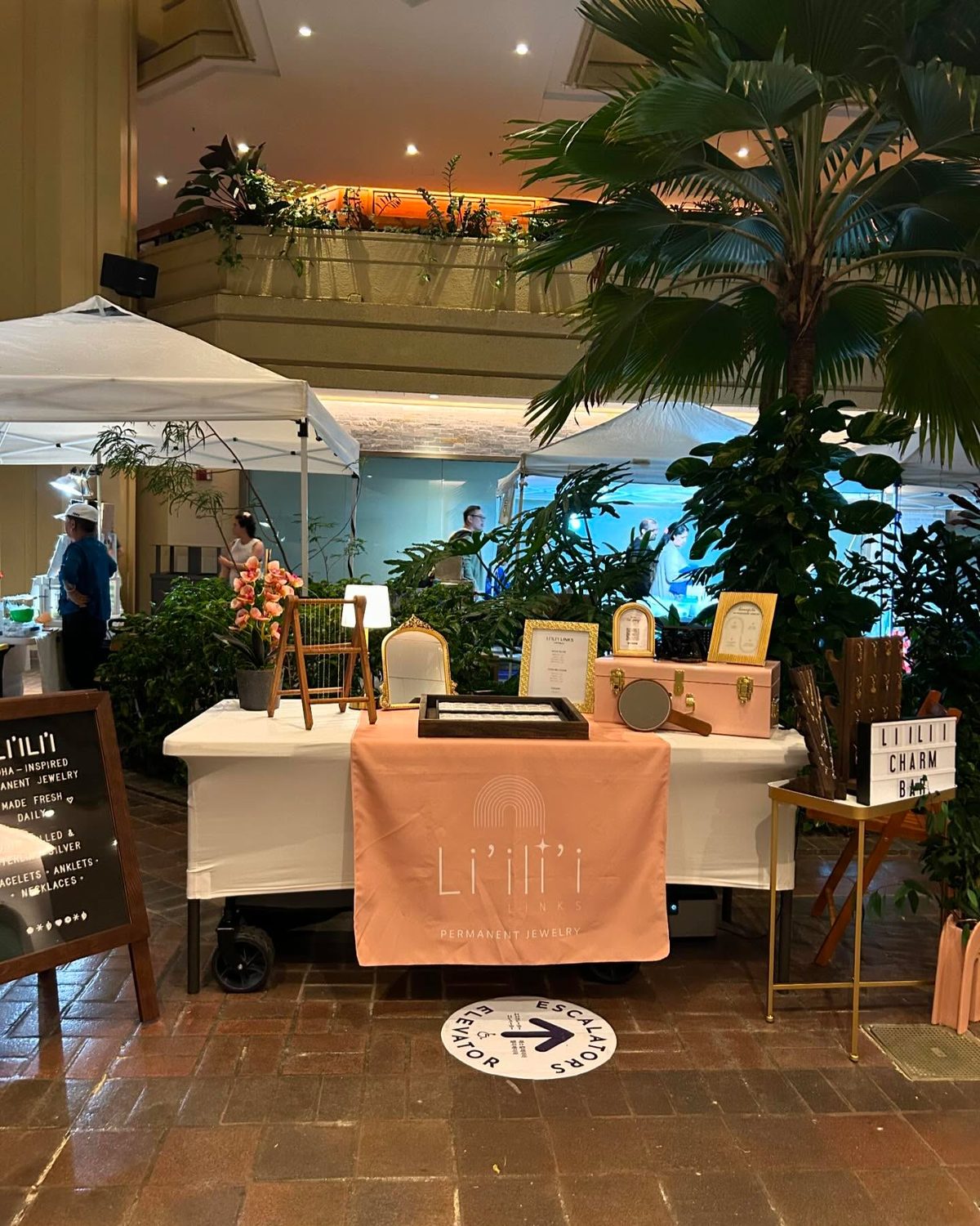 The Li'ili'i Links pop-up table with its blush pink logo cloth, set up on the ground floor of the Hyatt Regency Waikīkī